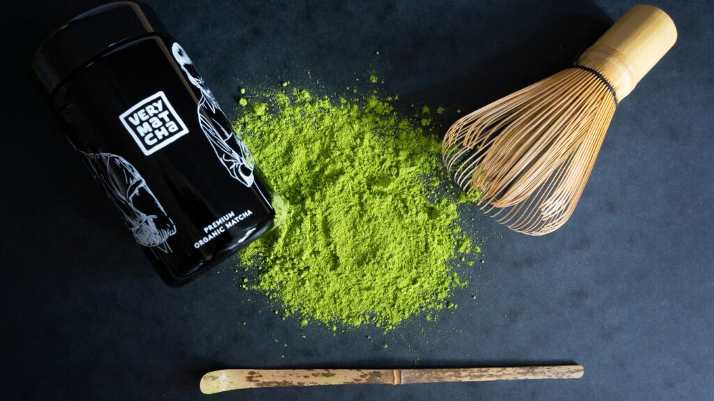 Matcha powder, whisk, and scoop on dark surface